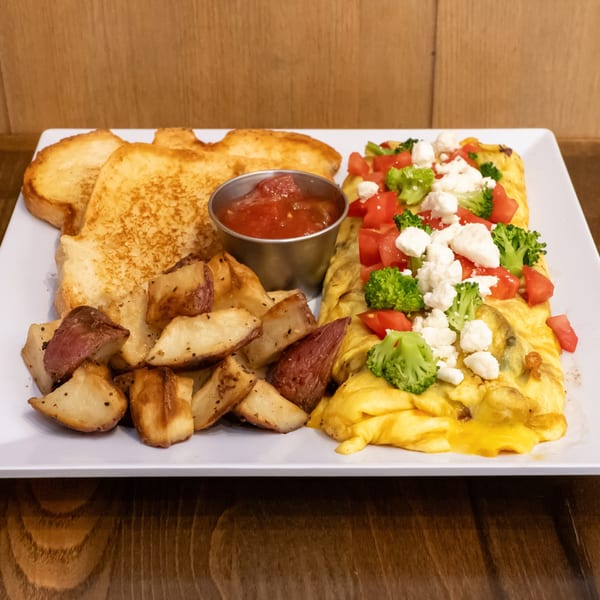 Platter of toast, roasted potatoes, cheesy omelets topped with broccoli, tomatoes, and feta, served with salsa.