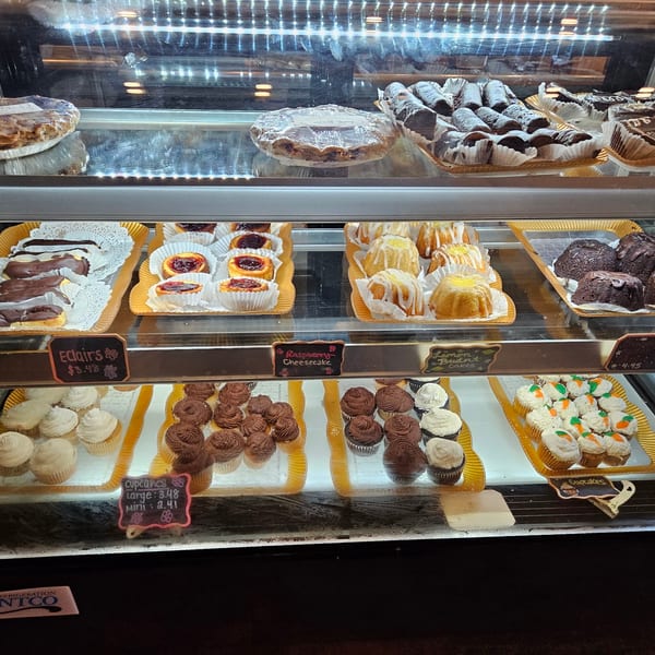 A brightly lit display case filled with various pastries, cakes, and cupcakes.