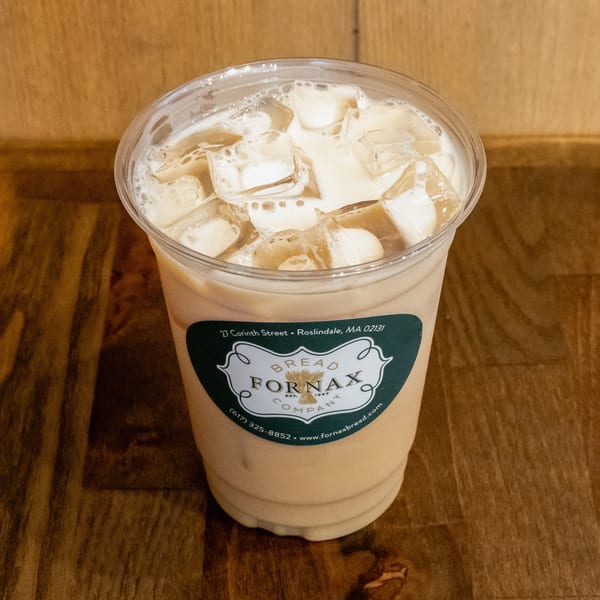 Iced creamy coffee drink in a clear cup labeled Bread Fornax, resting on a wooden table.