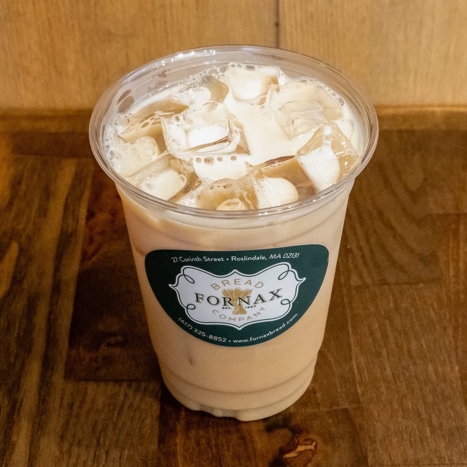 Iced creamy coffee drink in a clear cup labeled Bread Fornax, resting on a wooden table.