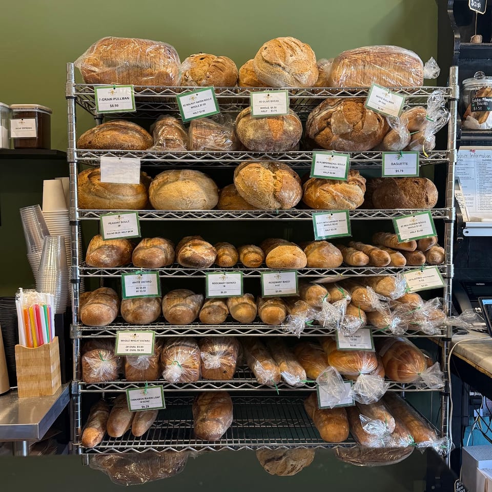 A bakery display rack filled with various freshly baked breads, loaves, and baguettes, many individually wrapped.
