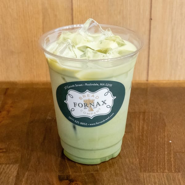 Iced pale green beverage in a clear Fornax Bread Company cup, resting on a wooden table.