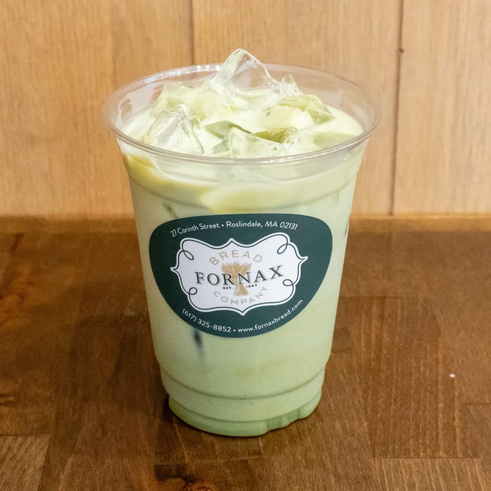 Iced pale green beverage in a clear Fornax Bread Company cup, resting on a wooden table.