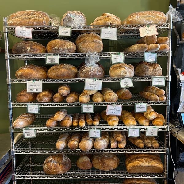 A metal shelving unit filled with various types of freshly baked bread loaves and baguettes.
