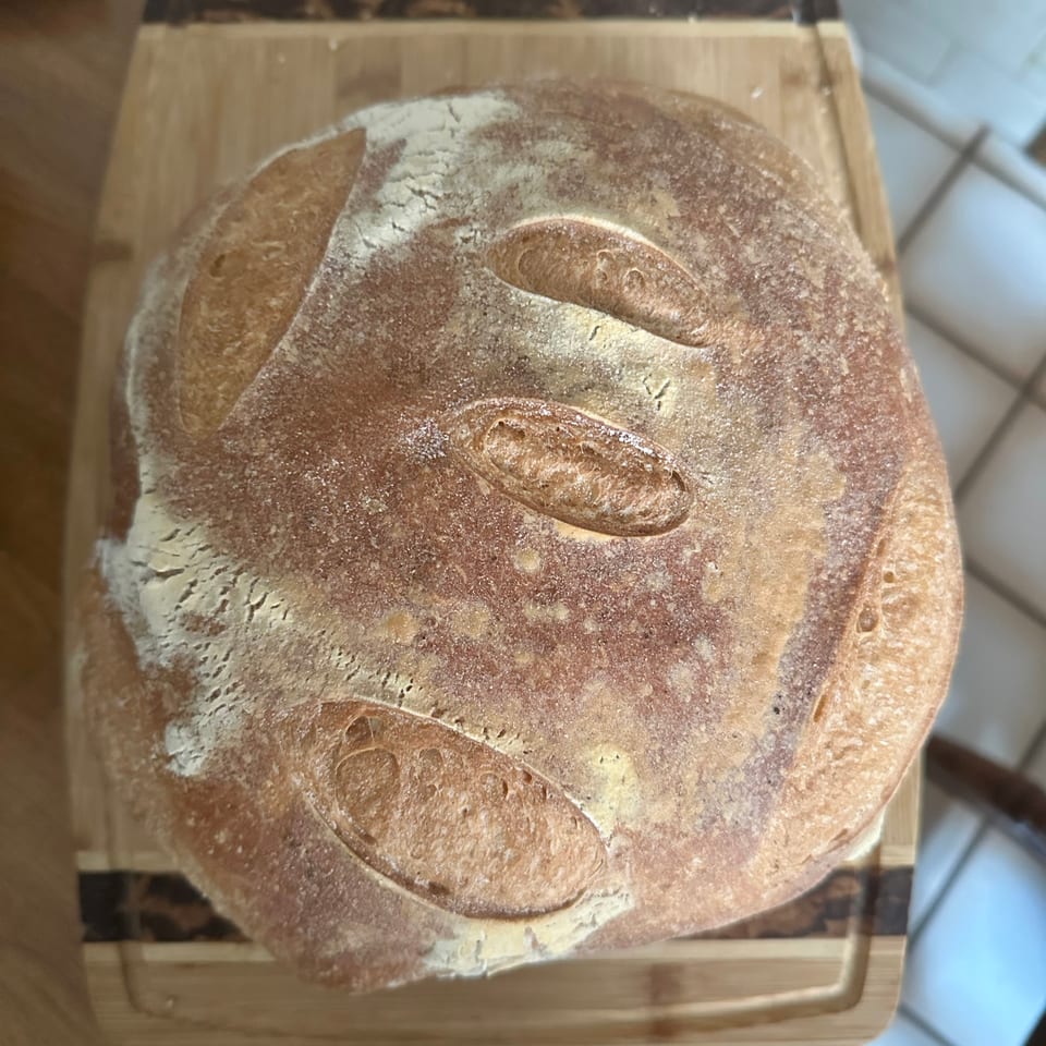 A freshly baked, round loaf of sourdough bread with a floured crust and scoring marks.